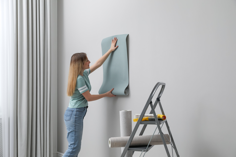 Chica joven muestra cómo poner papel pintado en la pared